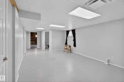 Expansive room featuring light gray walls, a dropped ceiling with integrated lighting, and painted concrete flooring - 110 52308 Rr 214, Rural Strathcona County, AB 