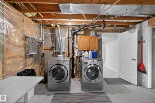 Dedicated laundry area featuring a front-load washer and dryer, exposed ceiling joists, and a utility sink - 110 52308 Rr 214, Rural Strathcona County, AB 