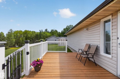 Expansive wood-finish deck featuring white railing with a black metal gate, beige siding, and a large exterior window - 110 52308 Rr 214, Rural Strathcona County, AB 