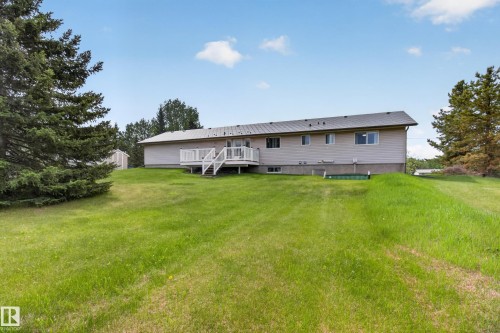 Rear exterior featuring a spacious lawn, large wood deck, siding facade, and a dark shingled roof - 110 52308 Rr 214, Rural Strathcona County, AB 