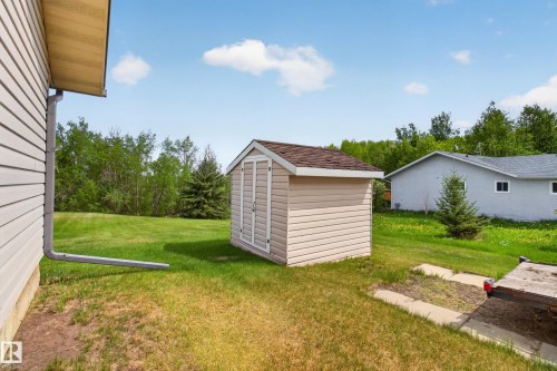Backyard featuring a tan vinyl-sided storage shed with a brown shingled roof, a manicured lawn, and mature trees - 110 52308 Rr 214, Rural Strathcona County, AB 