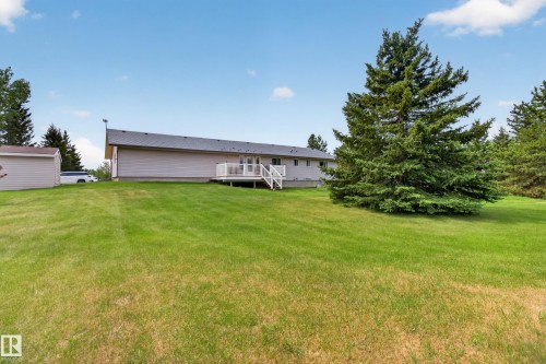 Rear exterior showcasing a spacious lawn, a wooden deck with white railings, and a large evergreen tree - 110 52308 Rr 214, Rural Strathcona County, AB 