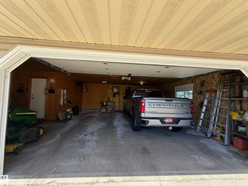 Attached garage with concrete flooring, wood-paneled walls, and a visible exterior door - 110 52308 Rr 214, Rural Strathcona County, AB 