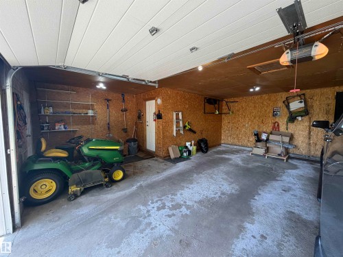 Concrete floor garage with exposed plywood walls, equipped with an automatic garage door opener, built-in shelving, a side access door, and recessed lighting - 110 52308 Rr 214, Rural Strathcona County, AB 
