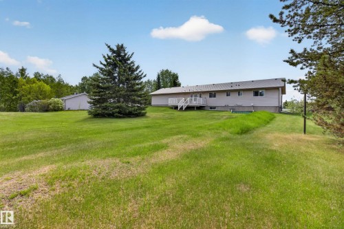 Spacious rear yard with a verdant lawn, mature pine tree, and a white deck featuring railing - 110 52308 Rr 214, Rural Strathcona County, AB 