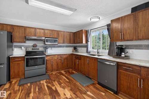 Kitchen featuring wood-finish flooring, wood cabinetry, light-toned countertops, stainless steel appliances, and a window with exterior scenery - 110 52308 Rr 214, Rural Strathcona County, AB 