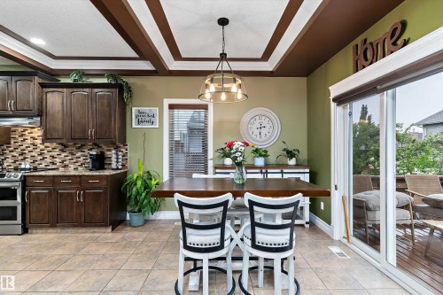 Kitchen and dining area featuring dark wood-finish cabinetry, a mosaic tile backsplash, and light-toned tile flooring - 16609 58A Street, Edmonton, AB 