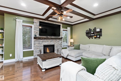Living area featuring wood-finish flooring, a stacked stone fireplace, and a wood beam coffered ceiling with a ceiling fan - 16609 58A Street, Edmonton, AB 