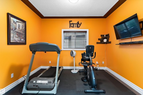 Dedicated room featuring a wall-mounted television, a built-in window with horizontal blinds, and dark-toned wall shelves - 16609 58A Street, Edmonton, AB 