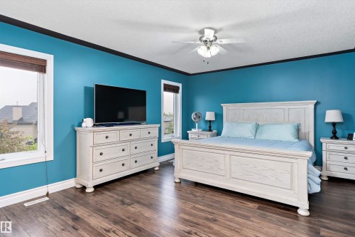 Spacious room featuring wood-finish flooring, two windows with blinds, a ceiling fan with light fixture, and crown molding - 16609 58A Street, Edmonton, AB 