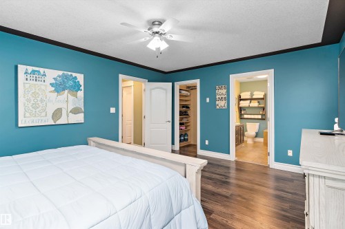 Bedroom featuring wood-finish flooring, a ceiling fan with integrated lighting, and a walk-in closet with built-in shelving - 16609 58A Street, Edmonton, AB 