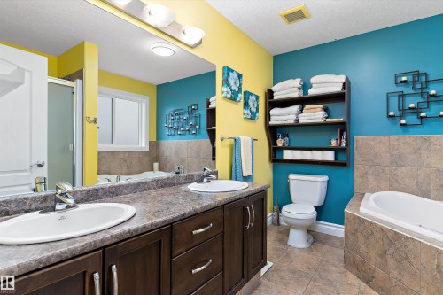 Bathroom featuring a double vanity with integrated sinks, a tiled shower enclosure, a built-in soaking tub with tile surround, and tile flooring - 16609 58A Street, Edmonton, AB 