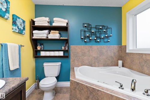 Bathroom featuring a built-in jetted tub with chrome fixtures, tiled tub surround, and a window for natural light - 16609 58A Street, Edmonton, AB 