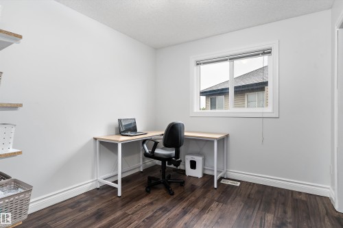 Room featuring wood-finish flooring, white baseboards, and a large window with blinds - 16609 58A Street, Edmonton, AB 
