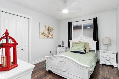 Bedroom featuring rich wood-finish flooring, a contemporary ceiling fan with integrated lighting, and a window with dark curtain rods - 16609 58A Street, Edmonton, AB 