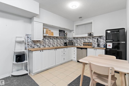 Kitchen featuring white cabinetry, wood-finish countertops, and a mosaic tile backsplash - 16609 58A Street, Edmonton, AB 