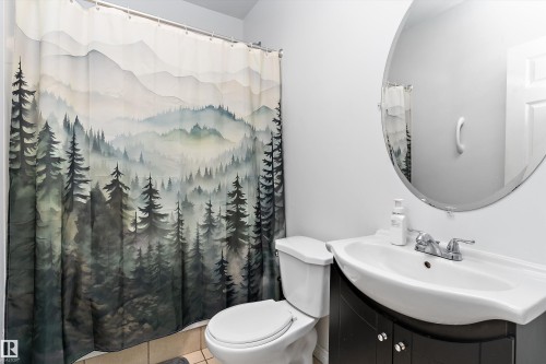 Bathroom with a white toilet, a vanity with a white basin sink, a chrome faucet, and an oval wall-mounted mirror - 16609 58A Street, Edmonton, AB 