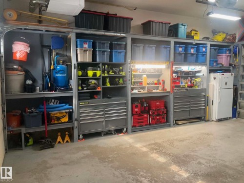 Concrete flooring with a comprehensive wall-mounted storage system, featuring integrated shelving, multiple cabinet units, and a built-in workbench with task lighting - 16609 58A Street, Edmonton, AB 
