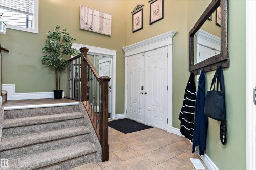 Foyer featuring a double entry door with decorative panels, tile flooring, and a carpeted staircase with wood and wrought iron railings - 16609 58A Street, Edmonton, AB 
