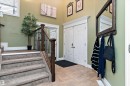 Foyer featuring a double entry door with decorative panels, tile flooring, and a carpeted staircase with wood and wrought iron railings - 16609 58A Street, Edmonton, AB 