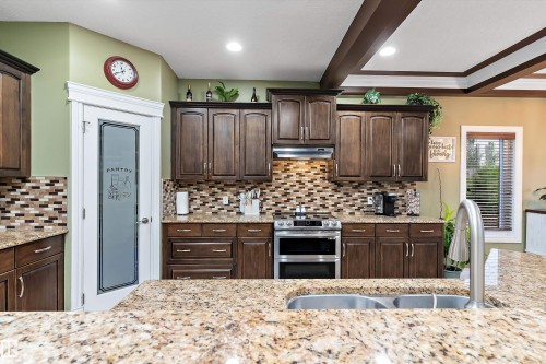 Kitchen featuring wood-finish cabinetry, granite countertops, and a full tile backsplash - 16609 58A Street, Edmonton, AB 