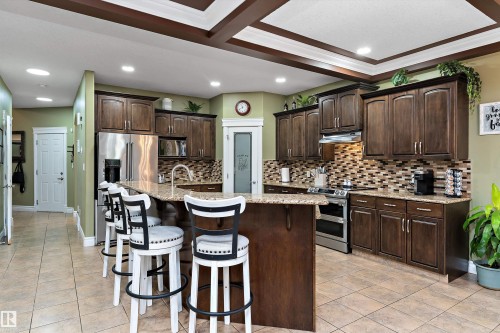 Kitchen featuring coffered ceilings, recessed lighting, wood-finish cabinetry, stainless steel appliances, and a tiled backsplash - 16609 58A Street, Edmonton, AB 