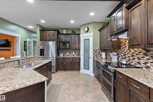 Kitchen featuring granite countertops, dark wood-finish cabinetry, stainless steel appliances, a mosaic tile backsplash, and ceramic tile flooring - 16609 58A Street, Edmonton, AB 