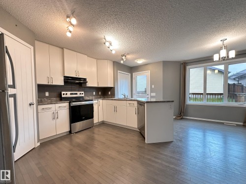 Kitchen and dining area featuring wood-finish flooring, white cabinetry, stainless steel appliances, and a gray subway tile backsplash - 9432 211 Street, Edmonton, AB 
