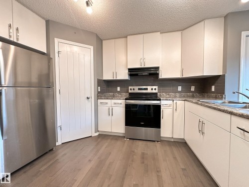 Modern kitchen featuring white cabinetry, stainless steel appliances, wood-finish flooring, and a dark tile backsplash - 9432 211 Street, Edmonton, AB 