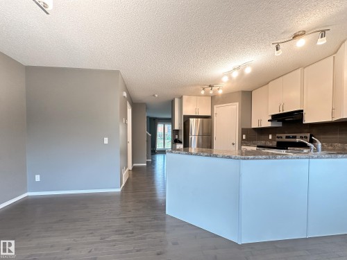 Contemporary kitchen featuring white cabinetry, stainless steel appliances, and a dark tiled backsplash - 9432 211 Street, Edmonton, AB 