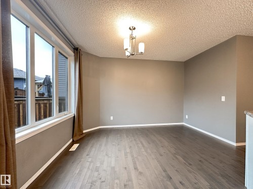 Spacious room featuring wood-finish flooring, neutral-toned walls, a multi-pane window, and a contemporary ceiling light fixture - 9432 211 Street, Edmonton, AB 