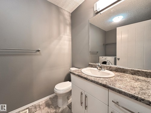 Bathroom featuring a white vanity with a patterned countertop, a built-in sink with a chrome faucet, and a large mirror - 9432 211 Street, Edmonton, AB 