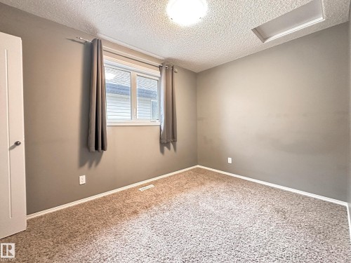 Carpeted interior space featuring a window with blinds, a white door, and a flush-mount ceiling light - 9432 211 Street, Edmonton, AB 