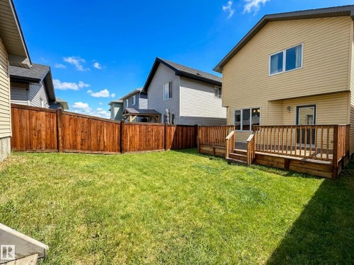 Expansive backyard featuring a manicured lawn, full wood privacy fence, and a multi-level wood deck with railing - 9432 211 Street, Edmonton, AB 