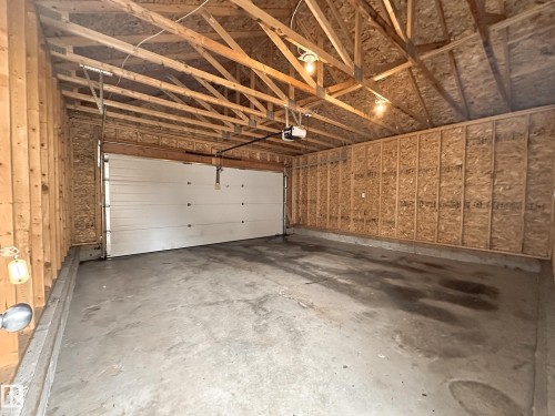 Garage interior featuring exposed wood framing, oriented strand board (OSB) walls, a concrete floor, and an overhead garage door with an automatic opener - 9432 211 Street, Edmonton, AB 