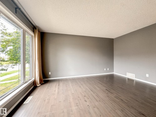 Expansive room featuring dark wood-finish flooring, neutral gray walls, and large picture windows - 9432 211 Street, Edmonton, AB 