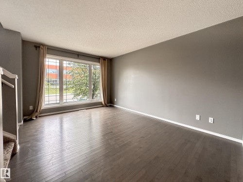 Spacious interior featuring wide-plank wood-finish flooring, a large multi-pane window, and neutral wall tones - 9432 211 Street, Edmonton, AB 