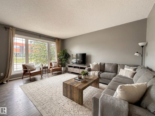 Spacious living area featuring large picture windows, wood-finish flooring, and light gray wall tones - 9432 211 Street, Edmonton, AB 
