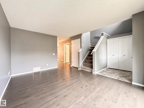 Spacious room featuring wood-finish flooring, neutral gray walls, white baseboards, and textured ceiling - 9432 211 Street, Edmonton, AB 