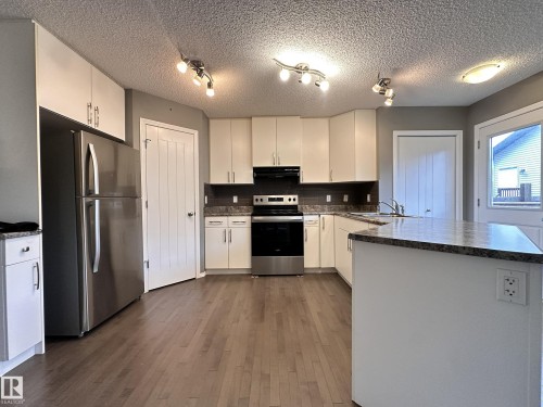 Modern kitchen featuring white cabinetry, stainless steel appliances, a center island with countertop, wood-finish flooring, and track lighting - 9432 211 Street, Edmonton, AB 