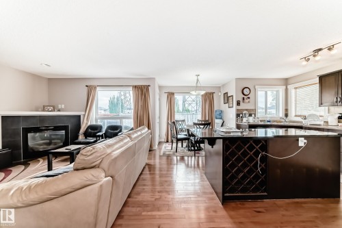 Open-concept living space featuring wood-finish flooring, a fireplace with a black tile surround, a kitchen island with a built-in wine rack, and dark wood cabinetry - 2808 36 Avenue, Edmonton, AB 
