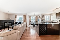 Open-concept living space featuring wood-finish flooring, a fireplace with a black tile surround, a kitchen island with a built-in wine rack, and dark wood cabinetry - 