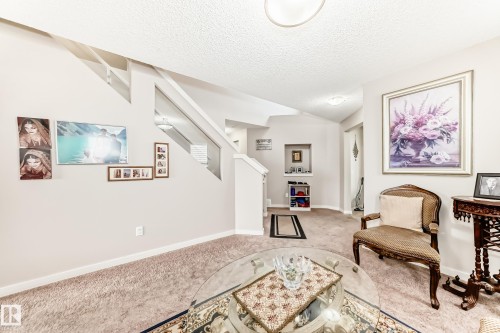Carpeted living area featuring a vaulted ceiling, wall recess, and a staircase with a white railing - 2808 36 Avenue, Edmonton, AB 