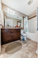 Bathroom featuring a wood-finish vanity with countertop, large wall mirror, and modern vanity lighting - 