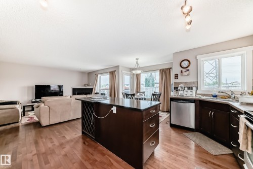 Open-concept living space featuring wood-finish flooring, a kitchen island with dark cabinetry and a dark countertop, stainless steel appliances, a tile backsplash, and recessed lighting - 2808 36 Avenue, Edmonton, AB 