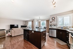 Open-concept living space featuring wood-finish flooring, a kitchen island with dark cabinetry and a dark countertop, stainless steel appliances, a tile backsplash, and recessed lighting - 