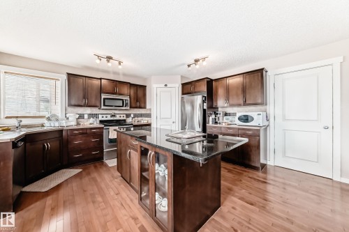 Kitchen featuring dark wood cabinetry, a central island with a dark countertop, wood-finish flooring, and stainless-steel appliances - 2808 36 Avenue, Edmonton, AB 