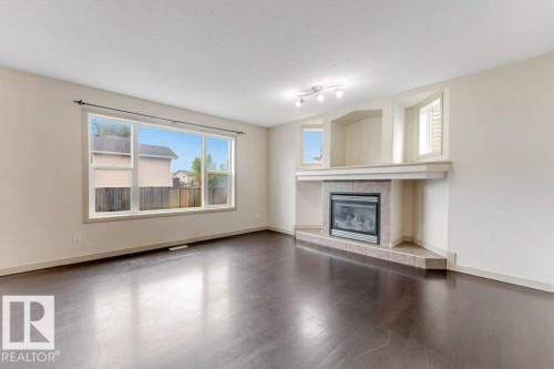 Spacious interior featuring dark wood-finish flooring, a large picture window, and a built-in fireplace with a tiled surround - 16315 55 Street, Edmonton, AB 