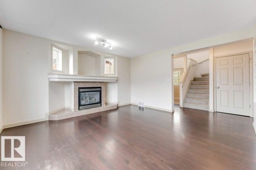 Living space featuring wood-finish flooring and a corner fireplace with a tile surround and mantel - 16315 55 Street, Edmonton, AB 