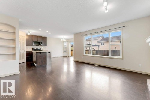 Open concept living area featuring dark wood-finish flooring, a kitchen island with integrated dishwasher, stainless steel appliances, and a built-in shelving unit - 16315 55 Street, Edmonton, AB 